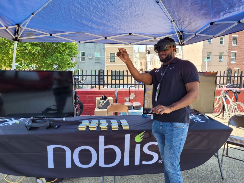 A black, male Noblis employee demos virtual reality glasses at a booth at the South Philly HIgh School Ram Fair for students in STEM.